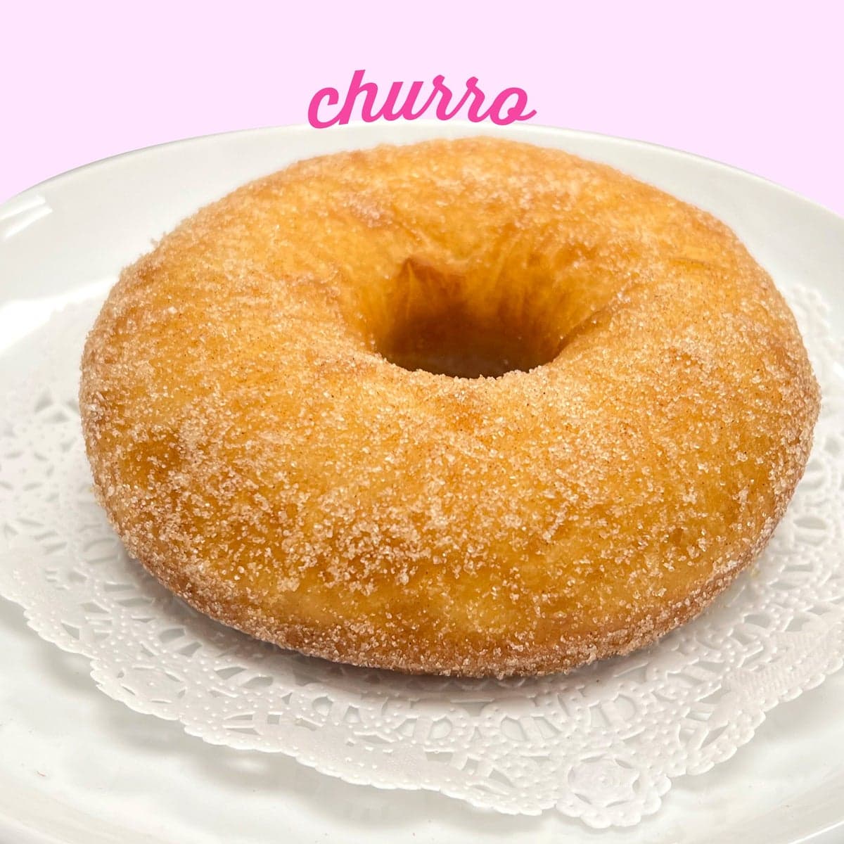 A churro doughnut rolled in cinnamon sugar on a paper doily
