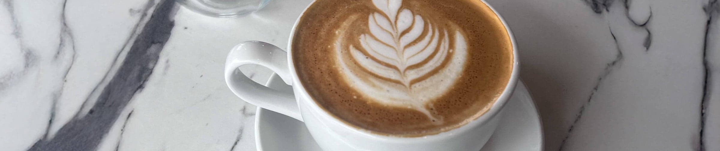 A latte poured with a leaf in the foam, on the marble counter at Viva La Fresa